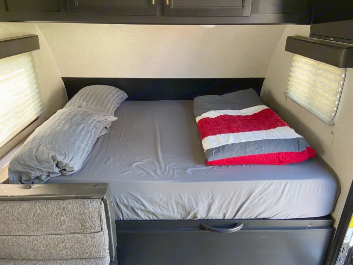 RV rental bed with grey sheets, two pillows, and a red, white, and grey sleeping bag ready for a cozy night's sleep.. Cherokee wolf pup 2021