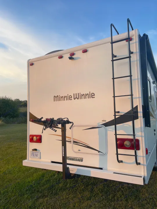 Back of a Winnebago Minnie Winnie RV rental with a Yakima bike rack, ladder, and Kentucky plate on grass under a clear sky.. Winnebago Minnie Winnie 2019
