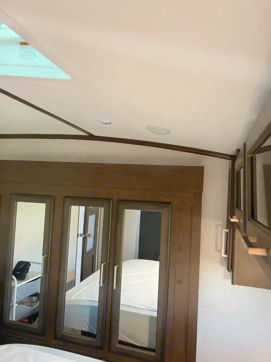 RV interior bedroom with dark wood mirrored cabinets, overhead storage, and a ceiling vent with a warning label. Great for an rv rental.. Atlas Atlas Fifth Wheel 2020