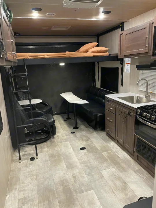 Spacious RV rental interior featuring an elevated bunk bed, flexible seating area, and a complete kitchen with a stove and sink.. Genesis Supreme Rv Genesis Supreme 2022