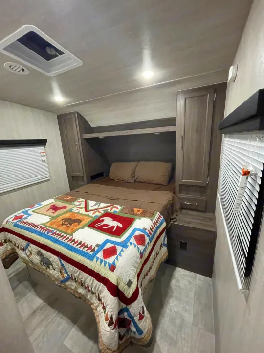 Cozy RV rental bedroom featuring a bed with a horse-themed quilt, built-in storage, and windows with blinds.. Genesis Supreme Rv Genesis Supreme 2022