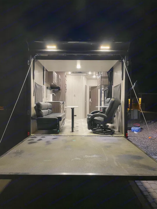 Inside an RV rental toy hauler: A comfy living space with sofa, kitchen, recliner, and the open ramp patio.. Genesis Supreme Rv Genesis Supreme 2022