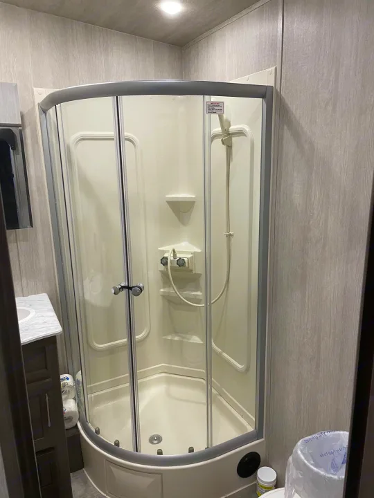 Compact RV rental bathroom featuring a corner shower and sink area with light wood-patterned walls.. Genesis Supreme Rv Genesis Supreme 2022