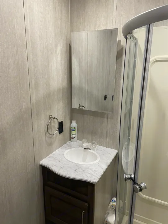 Compact RV rental bathroom: light wood-look walls, white sink vanity, mirrored cabinet, and curved glass shower stall.. Genesis Supreme Rv Genesis Supreme 2022