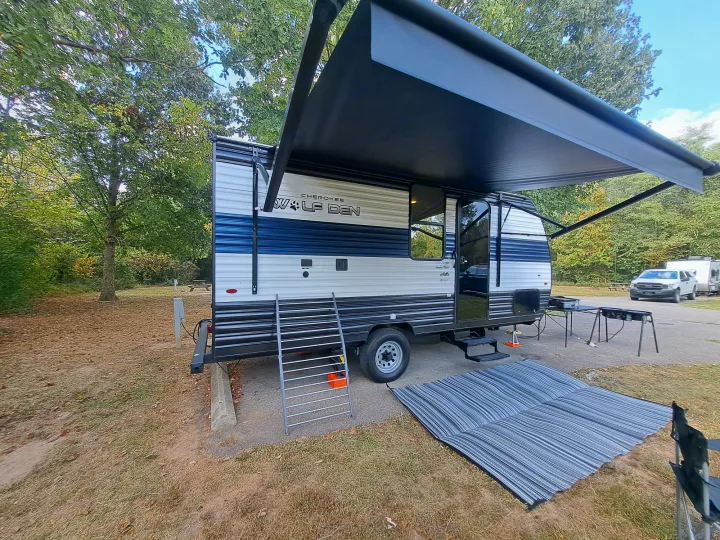 Cherokee Wolf Den RV rental set up at a campsite with awning extended, mat, and outdoor kitchen. Perfect for camping.. Forest River Cherokee 2024