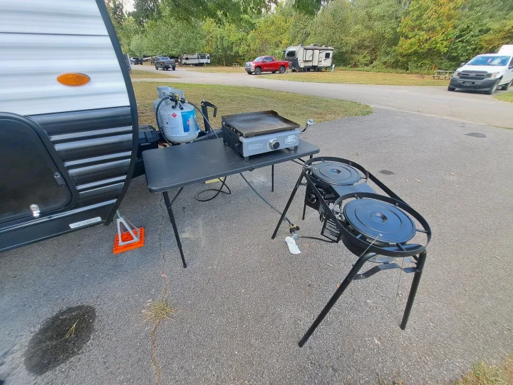RV rental campsite showing travel trailer, propane tank, griddle, and twin burners setup for outdoor cooking.. Forest River Cherokee 2024