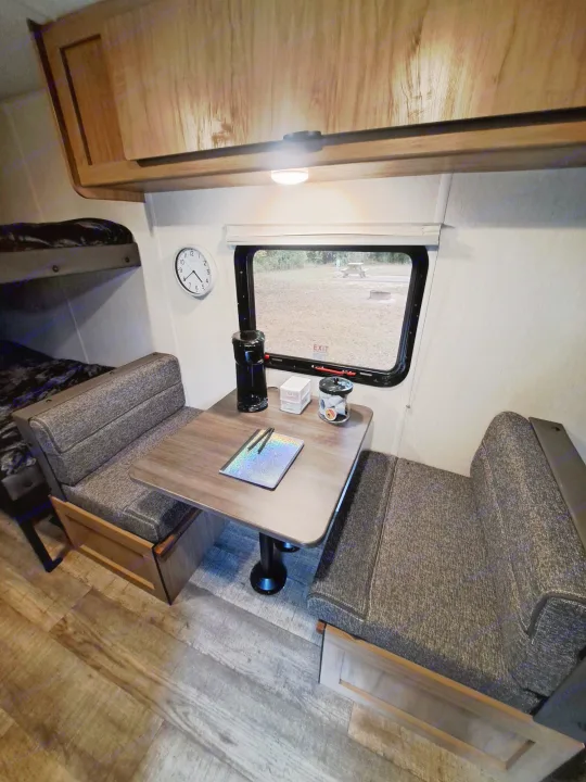 Compact RV rental interior featuring a cozy dinette, bunk beds, and a view of the campsite.. Forest River Cherokee 2024