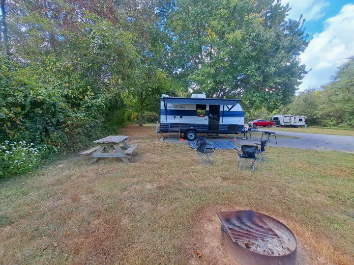 Serene RV rental campsite: blue & white travel trailer, picnic table, chairs, & fire pit. Perfect for a peaceful camping trip.. Forest River Cherokee 2024