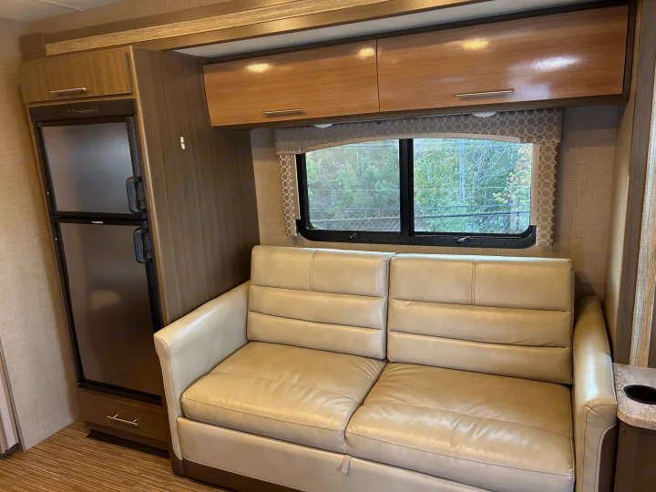 Experience comfort in this RV rental's living area, featuring a tan sofa, Dometic fridge, and wood-look overhead cabinets.. Thor Axis 2018
