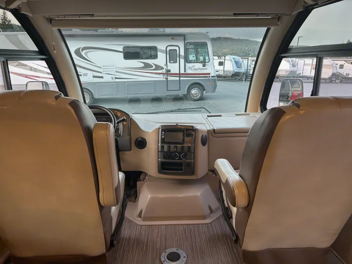 Spacious RV rental interior cockpit with dashboard, front seats, and view of other motorhomes.. Thor Axis 2018