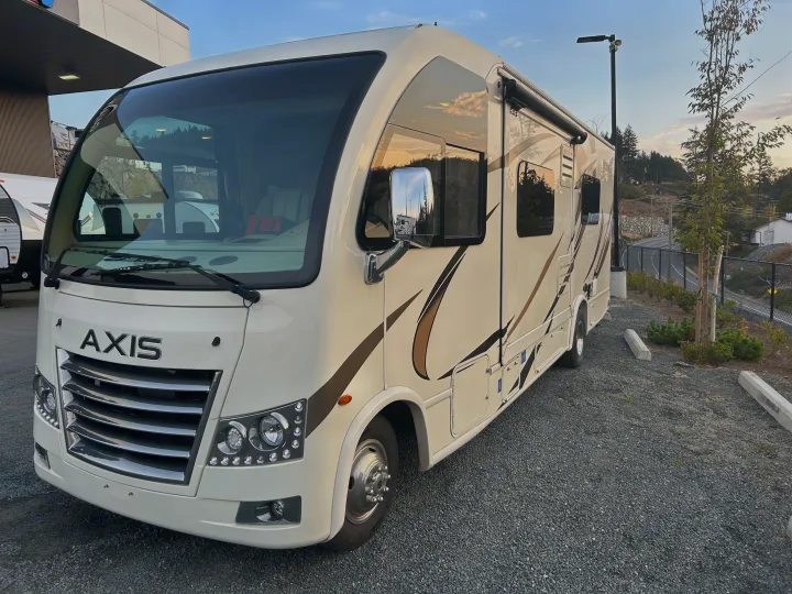 Front view of a cream Thor Axis motorhome on a gravel lot, suitable for RV rental, with "AXIS" branding visible.. Thor Axis 2018