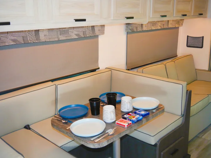 RV rental dinette setup: a bright interior with comfortable seating, a set table for dining or games, and pull-down window blinds.. Forest River Sunseeker Classic 2023