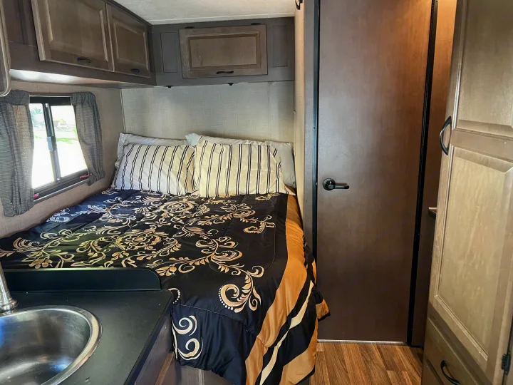 Cozy **RV rental** interior with a patterned bed, overhead cabinets, window, and a small sink for convenience.. Thor Majestic 2019