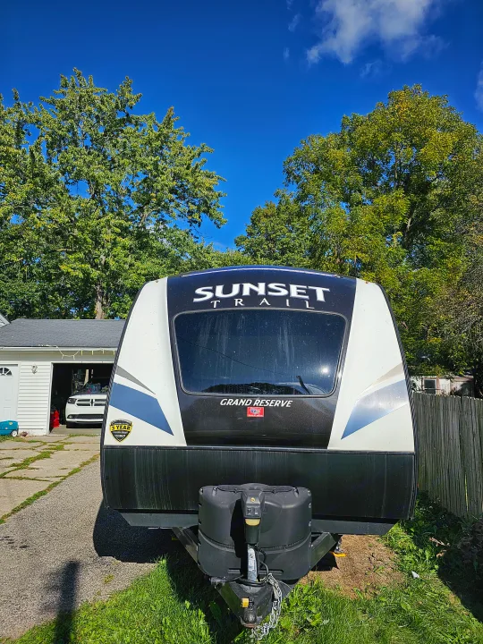 A white and black Sunset Trail Grand Reserve travel trailer, parked outdoors near trees and a garage. Great for an rv rental!. Crossroads RV Sunset Trail Grand Reserve 2018