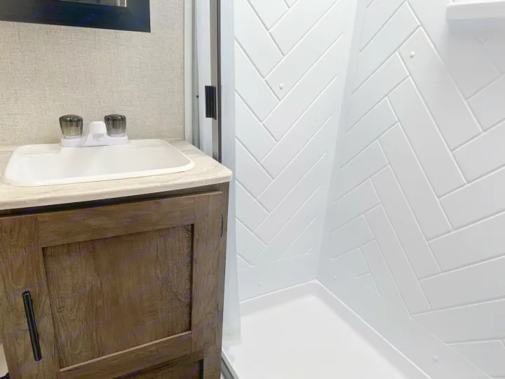 This modern RV rental bathroom features a vanity with a sink and a sleek shower with white herringbone walls.. Forest River Salem Cruise Lite 2021