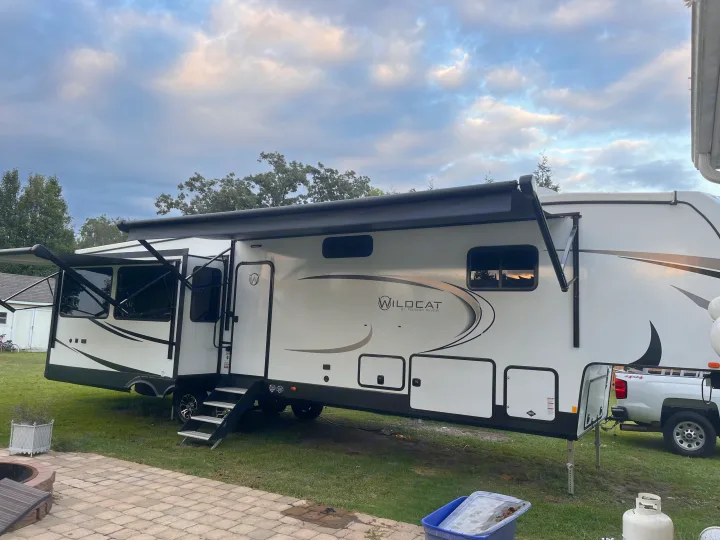 A large white Wildcat RV, a perfect rv rental, parked on grass with awnings extended and steps down, ready for use.. Forest River Wildcat 2023