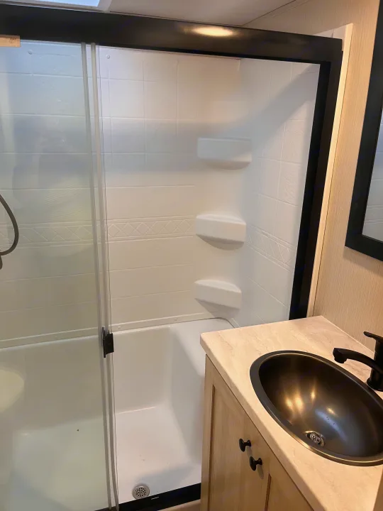 RV rental: Bright, compact bathroom with shower/tub, built-in shelving, and dark sink on a light vanity.. Forest River Wildcat 2023