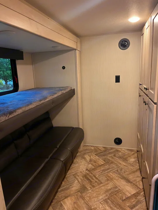 RV rental interior features bunk bed, sofa, light-toned cabinets, and herringbone floor pattern.. Forest River Wildcat 2023
