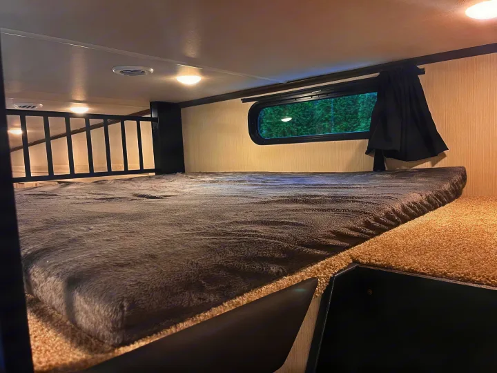 Inside an RV rental: a cozy bunk bed with a gray blanket, small window, and protective railing.. Forest River Wildcat 2023