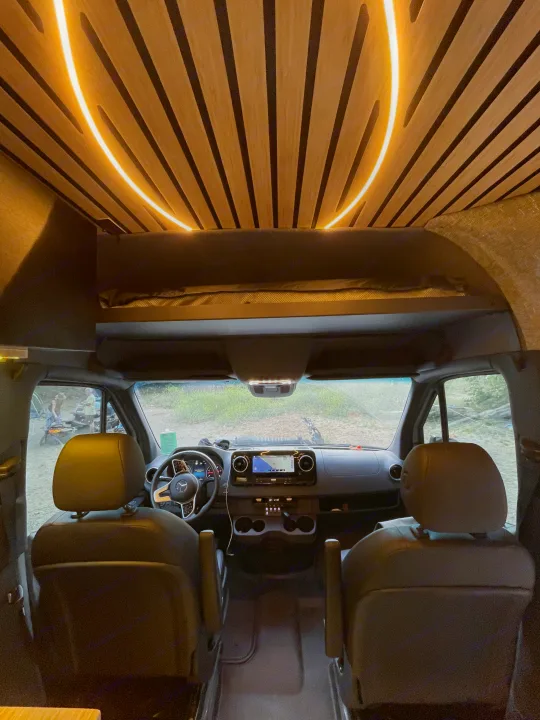 Experience comfort in this RV rental: unique wooden ceiling with curved LED lighting, modern front cabin, and a view of the outdoors.. Mercedes-Benz Sprinter RV Motorhome Campervan 2020