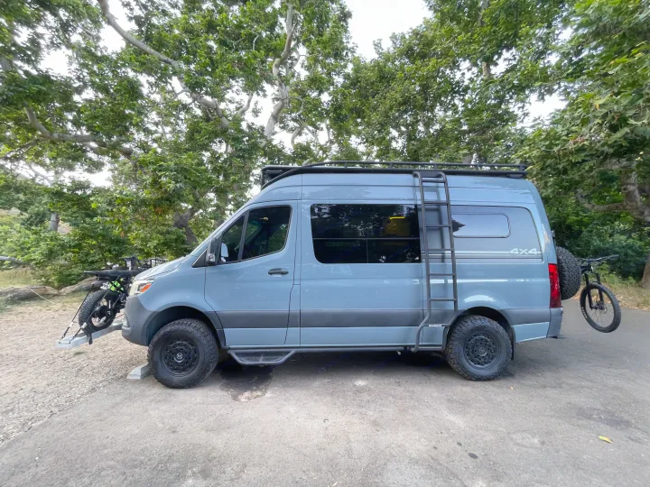 A grey 4x4 Sprinter camper van, equipped with bikes and roof rack, parked outdoors. Great for rv rental adventures.. Mercedes-Benz Sprinter RV Motorhome Campervan 2020