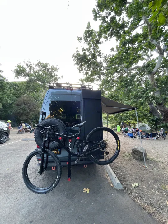 Adventure-ready RV rental with bike rack at a lively campsite, perfect for outdoor enthusiasts.. Mercedes-Benz Sprinter RV Motorhome Campervan 2020