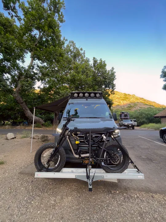 RV rental ready for adventure! Camper van with an electric motorcycle on a hitch carrier at a scenic campsite.. Mercedes-Benz Sprinter RV Motorhome Campervan 2020