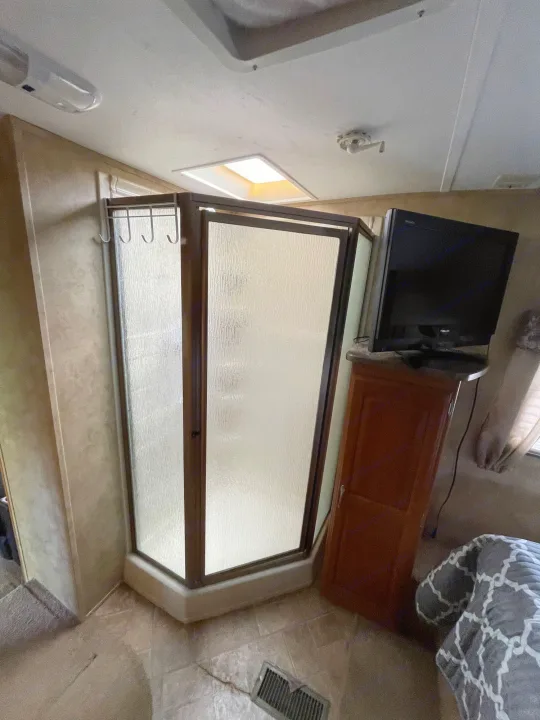 This RV rental's clever interior includes a compact corner shower with frosted glass, TV setup, and cozy bedroom area.. Keystone RV Cougar 2012