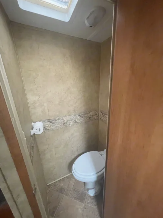 Compact RV rental bathroom with toilet, TP holder, tiled walls, and ceiling skylight.. Keystone RV Cougar 2012