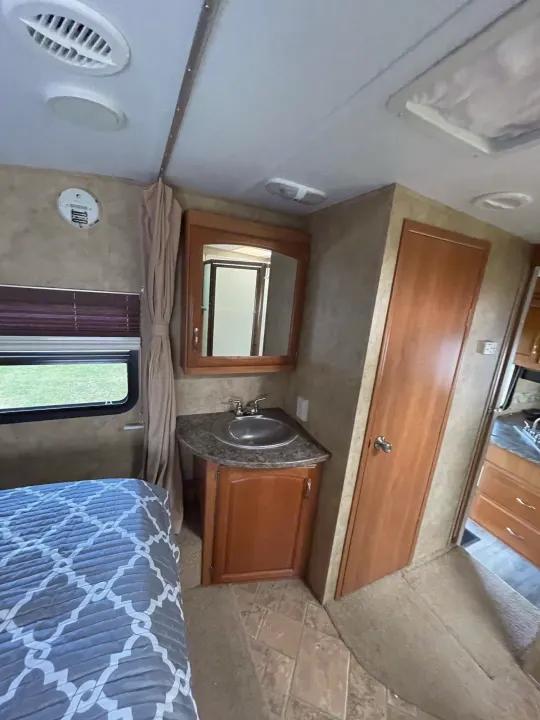 Experience comfort in this RV rental! View of the bedroom with patterned bed and adjacent vanity with sink and mirror.. Keystone RV Cougar 2012