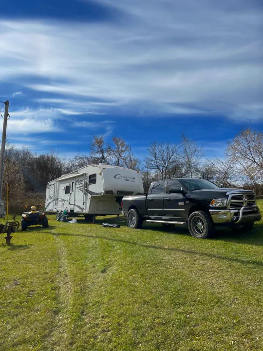 Black truck and large fifth-wheel RV parked on grass with an ATV. Ideal outdoor setup for an RV rental adventure.. Keystone RV Cougar 2012