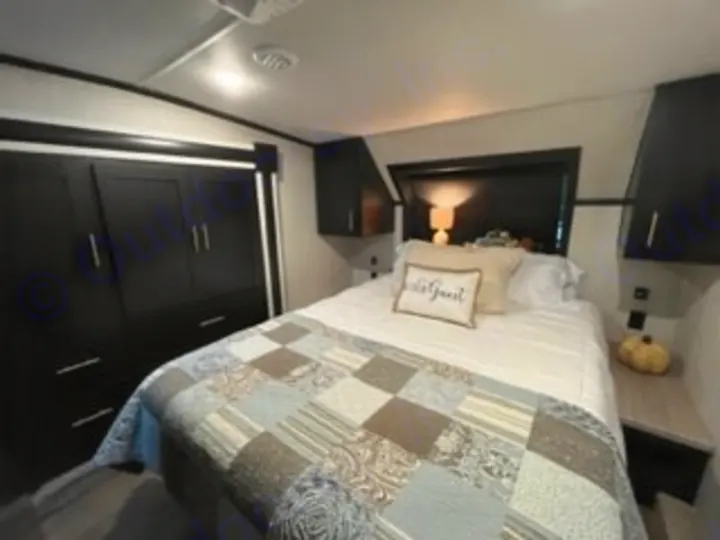 Comfortable RV rental bedroom featuring a queen bed with quilt, nightstands, and dark storage cabinets. Ready for your travels!. Forest River Wildcat 2022