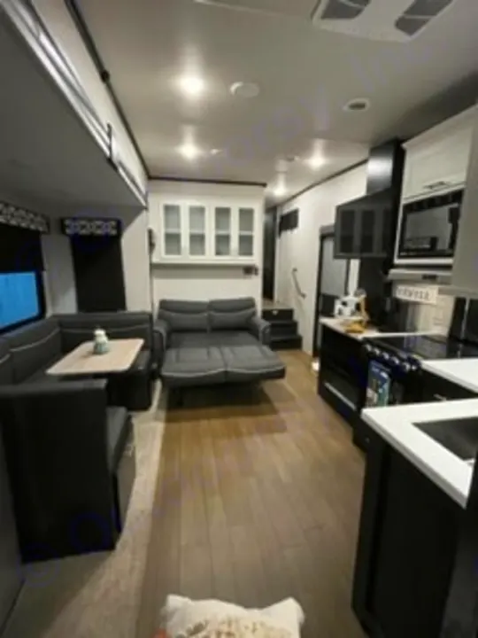 This modern RV rental interior features a spacious living area with a dark dinette, pull-out sofa, and full kitchen on wood floors.. Forest River Wildcat 2022