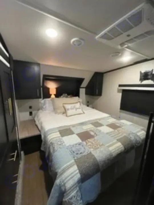 Cozy RV rental bedroom with a queen bed, dark wood cabinetry, and soft overhead lighting. Perfect for comfortable travel.. Forest River Wildcat 2022