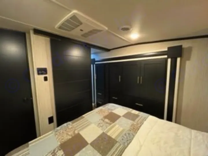 This RV rental's compact bedroom features dark cabinetry, a bed with a quilt, and a ceiling AC unit, perfect for travel.. Forest River Wildcat 2022
