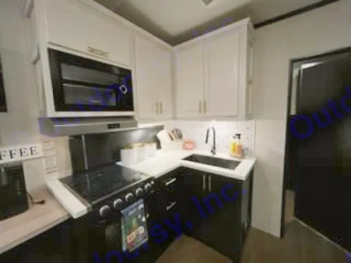 Inside this RV rental: a sleek, modern kitchen with black base cabinets, white uppers, stove, microwave, and sink.. Forest River Wildcat 2022