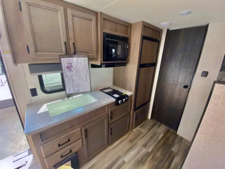 RV rental kitchen: light wood cabinets, sink, stove, microwave, and fridge. Ideal for road trip travel.. Starcraft Autumn Ridge 2023