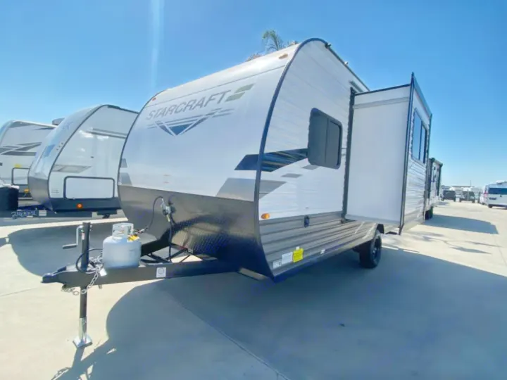 A white and grey Starcraft travel trailer with an extended side slide-out is parked on asphalt. Ideal for RV rental trips.. Starcraft Autumn Ridge 2023