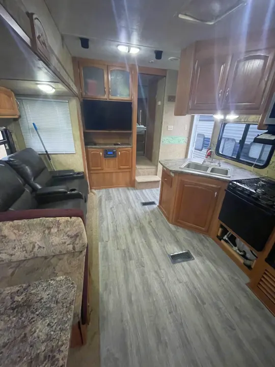 RV rental interior view: Recliner sofa, entertainment center, full kitchen with sink/stove, and wood-look flooring.. Keystone RV Cougar 2012