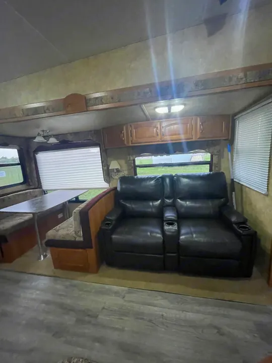 RV rental interior: Dinette, black reclining theater seating with cupholders, and outdoor views through windows.. Keystone RV Cougar 2012