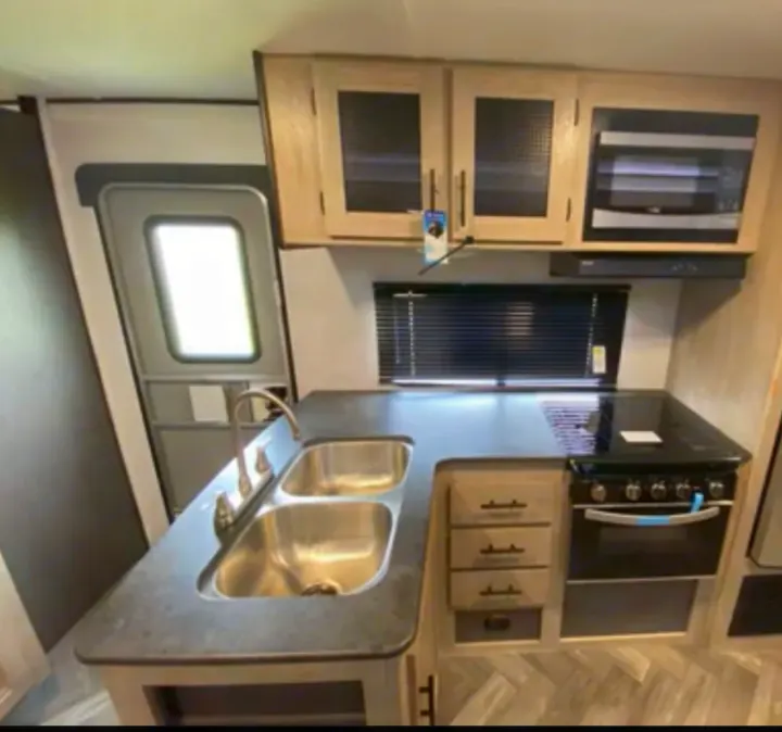 RV rental kitchen: Features a double sink, modern stove, microwave, and light wood cabinetry with dark countertops.. Heartland RVs Prowler 2022