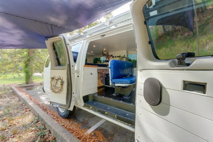 This custom RV rental camper van features an open side door, extended awning, blue passenger seat, and cozy interior.. Ford Ford E350 2007