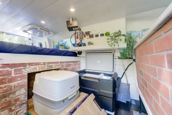 Compact RV rental interior: elevated bed, portable toilet, fridge, and built-in amenities in a converted van.. Ford Ford E350 2007