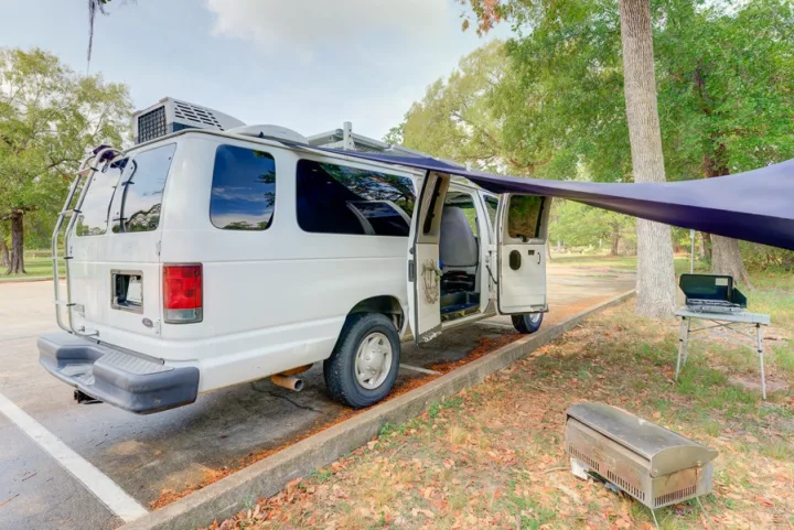 White camper RV rental with side awning, portable stove, and grill ready for outdoor cooking in a nature setting.. Ford Ford E350 2007