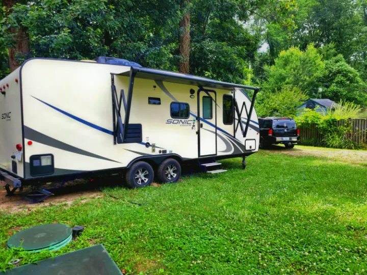 Experience outdoor living with this Sonic RV rental travel trailer parked on a green lawn beside an SUV.. Sonic Sonic Trailer 2019