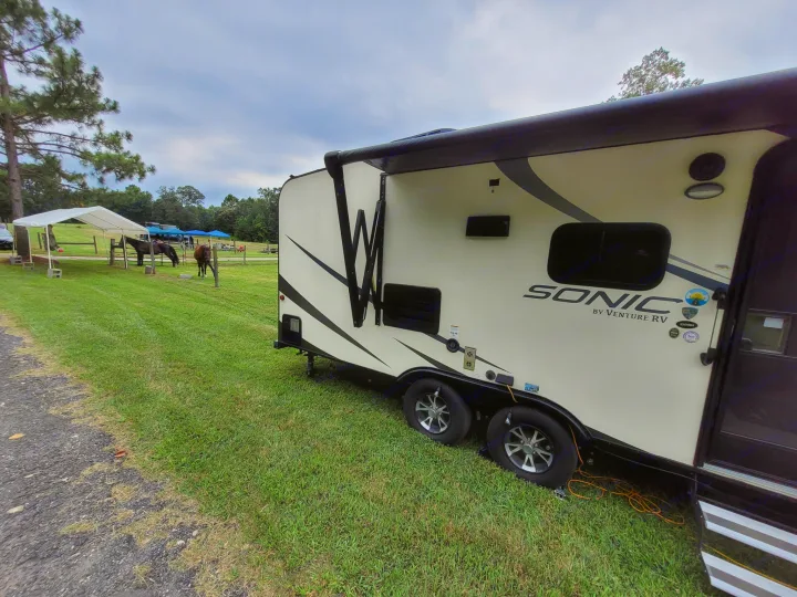 RV rental travel trailer with awning deployed, parked on grass at a serene campsite with horses grazing.. Sonic Sonic Trailer 2019