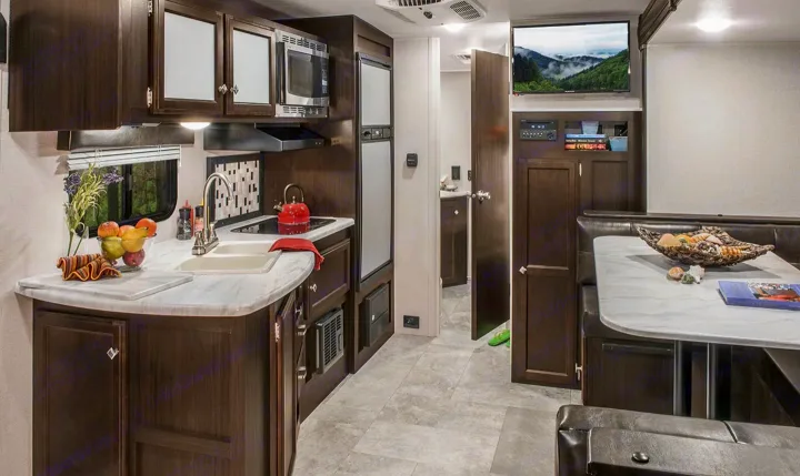 Modern RV rental interior with dark wood kitchen, sink, microwave, and a dinette living area with TV.. Sonic Sonic Trailer 2019