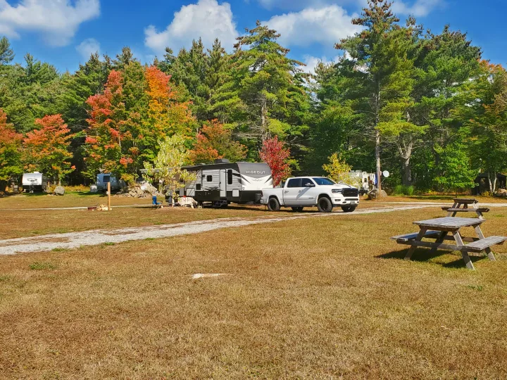 Discover autumn camping with an RV rental! A white truck is parked with a travel trailer at a fall campsite with picnic tables.. Keystone RV Hideout Luxury 2021