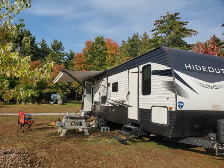 An RV rental, a white and black Hideout travel trailer, set up at a scenic autumn campsite with a dog and picnic area.. Keystone RV Hideout Luxury 2021