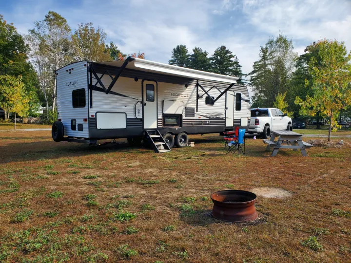 White Hideout RV rental parked at a sunny campsite with a pickup truck, picnic table, and fire pit, ready for camping.. Keystone RV Hideout Luxury 2021